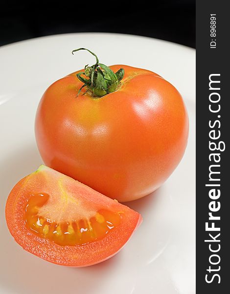 Red tomato and tomato slice on white plate with black background. Red tomato and tomato slice on white plate with black background