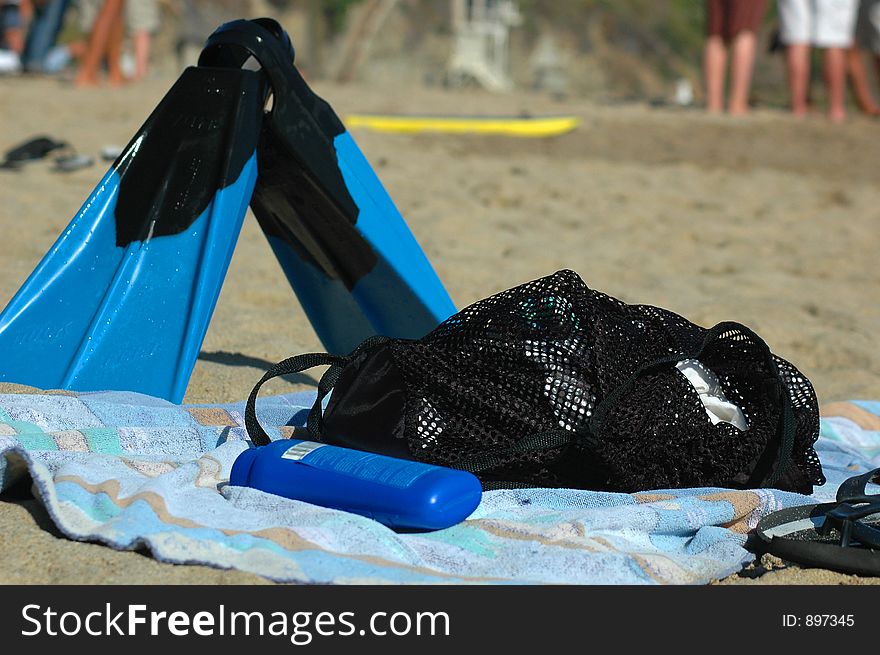 Sunscreen, fins, towel laying on a sandy beach waiting for their use. Sunscreen, fins, towel laying on a sandy beach waiting for their use