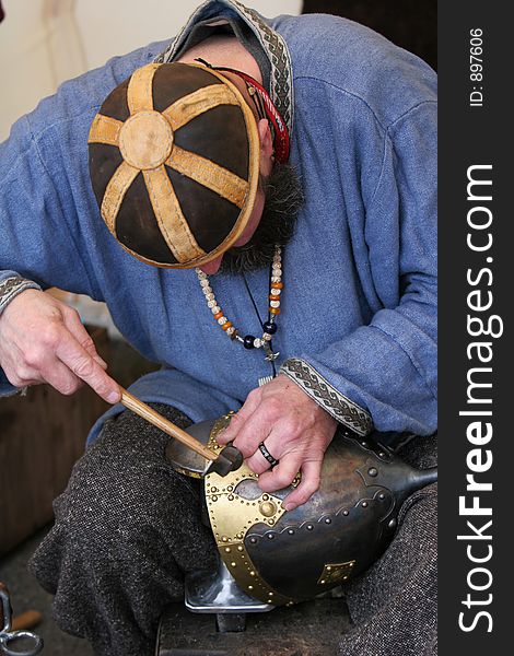 A craftsman chiseling inscription into a medieval soldiers helmet. A craftsman chiseling inscription into a medieval soldiers helmet