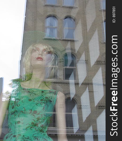 This image depicts a mannequin in a store window with the buildings across the street reflected. This image depicts a mannequin in a store window with the buildings across the street reflected.