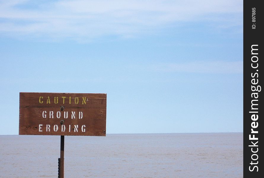 This image depicts a sign near the water's edge stating Caution: Ground Eroding,