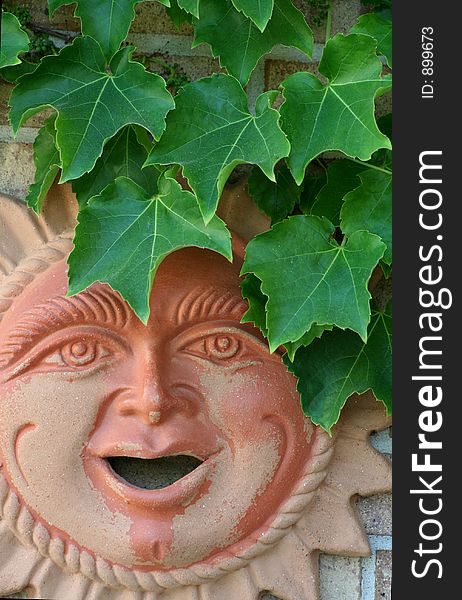 A terra cotta wall hanging of a sun faced man with leaves