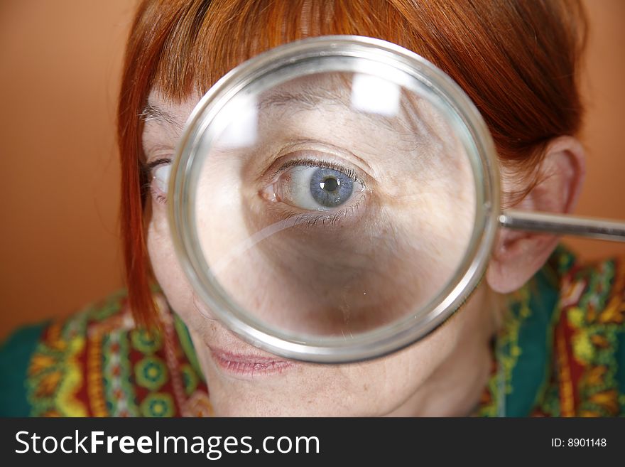 Red haired woman with blue eye peering through a magnifying glass. Red haired woman with blue eye peering through a magnifying glass