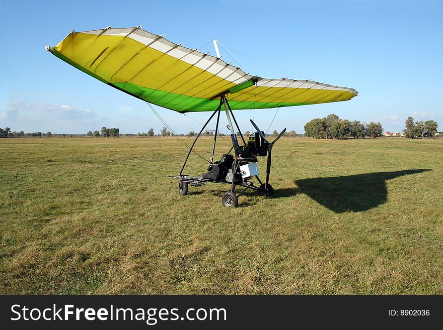 Yellow and green microlight on the field and its shadow on grass. Yellow and green microlight on the field and its shadow on grass