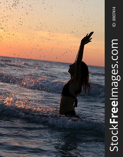 Woman splashing by sunset in the caribbean ocean