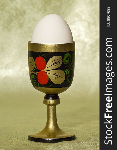 White egg in a wooden stand with a picture on a green background