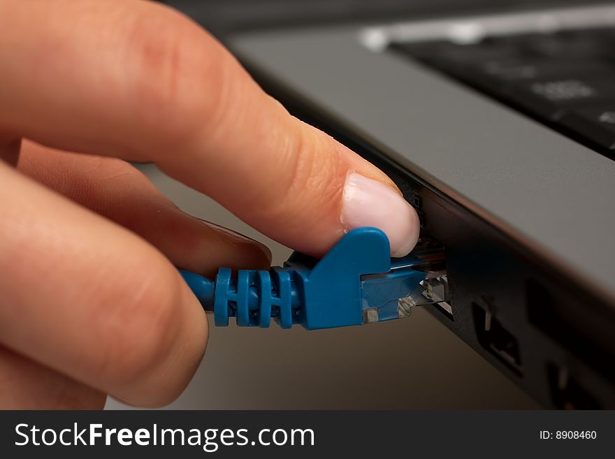 Female hand inserting a blue networking ethernet cable into a laptop. Female hand inserting a blue networking ethernet cable into a laptop