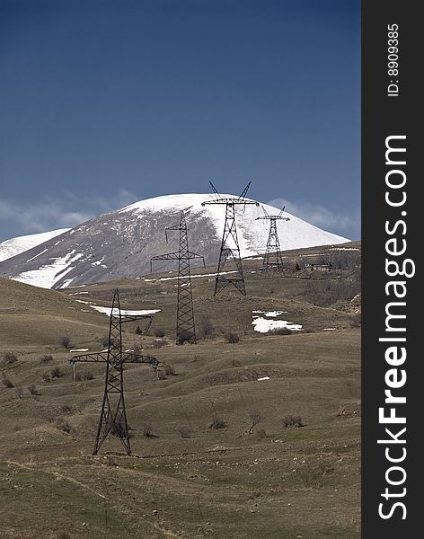 Electric line towers with snowy mountains in background. Electric line towers with snowy mountains in background.