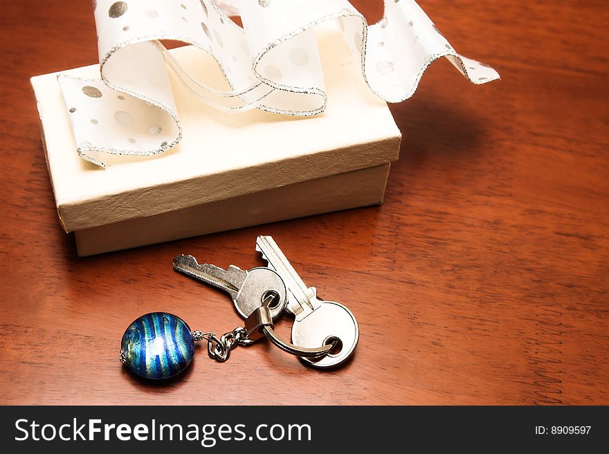 Two keys lying next to a cream colored gift box