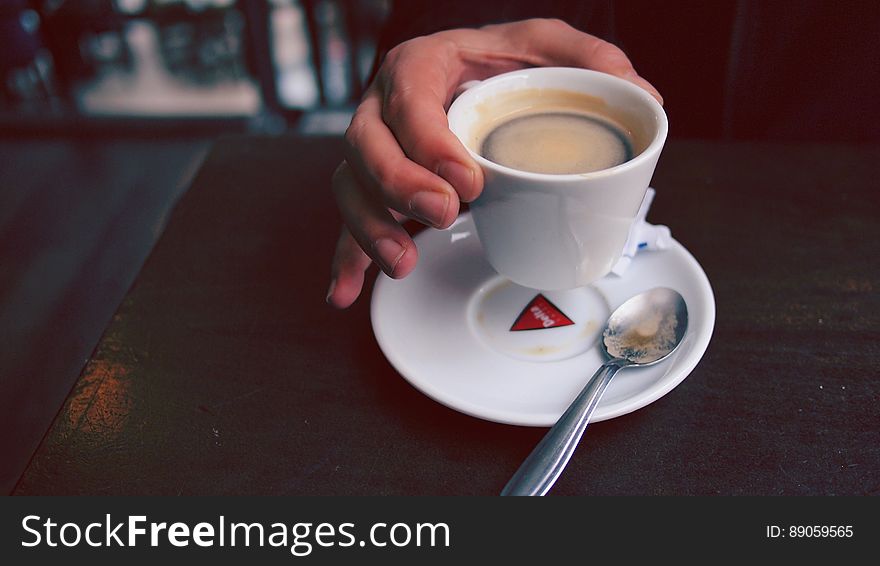 Hand of a person lifting cup of espresso coffee from saucer. Hand of a person lifting cup of espresso coffee from saucer.