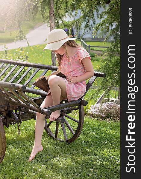 A girl sitting on an old wooden cart reading a book. A girl sitting on an old wooden cart reading a book.