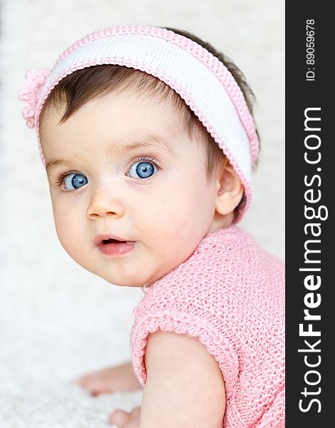 A baby with blue eyes and pink knitted headband and vest.