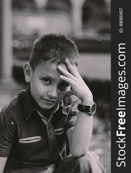 Black and white portrait of cute young boy outdoors with hand on forehead.