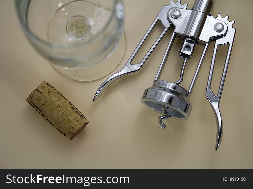 A wine cork has just been taken out and sits next to a wine glass and corkscrew. A wine cork has just been taken out and sits next to a wine glass and corkscrew.