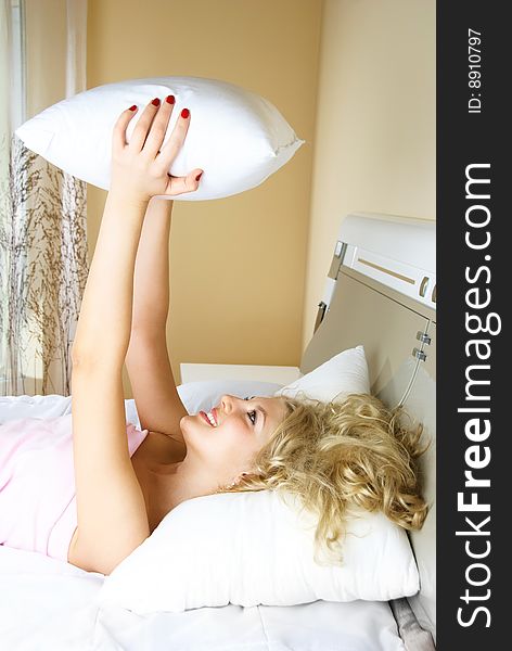 Beautiful young blond woman at home in bed bed with a pillow in her hands. Beautiful young blond woman at home in bed bed with a pillow in her hands