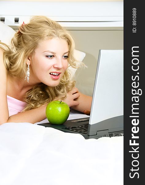 Beautiful girl at home on the bed using a laptop and eating a green apple. Beautiful girl at home on the bed using a laptop and eating a green apple
