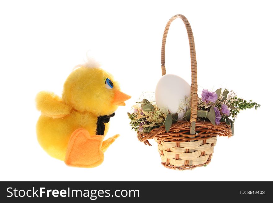 Toy chicken looks at the egg in the basket filled with small dry flowers
