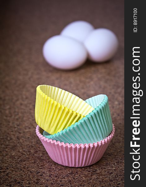 Pastel colored cupcake holders in foreground with three eggs out of focus in background