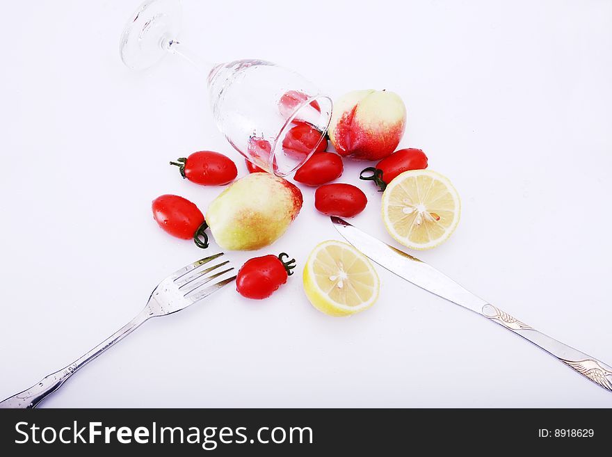 Peachs , peper , lemon and tomatoes on white background with goblet, water in it, knife and fork on desk. Peachs , peper , lemon and tomatoes on white background with goblet, water in it, knife and fork on desk