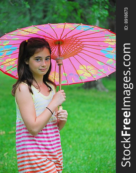 Beautiful 10 year old brown haired girl holding a parasol outdoors in the park. Beautiful 10 year old brown haired girl holding a parasol outdoors in the park