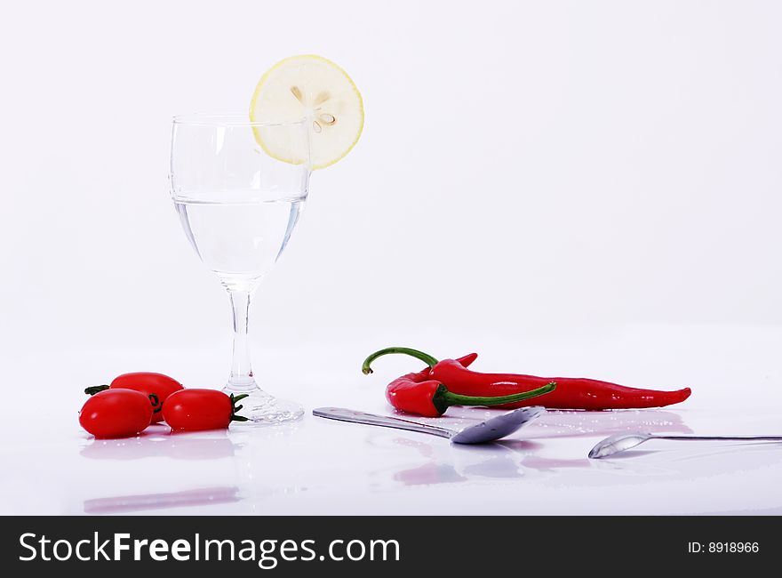 Peper and tomatoes, lemon on white background with goblet, water in it, spoon on desk. Peper and tomatoes, lemon on white background with goblet, water in it, spoon on desk