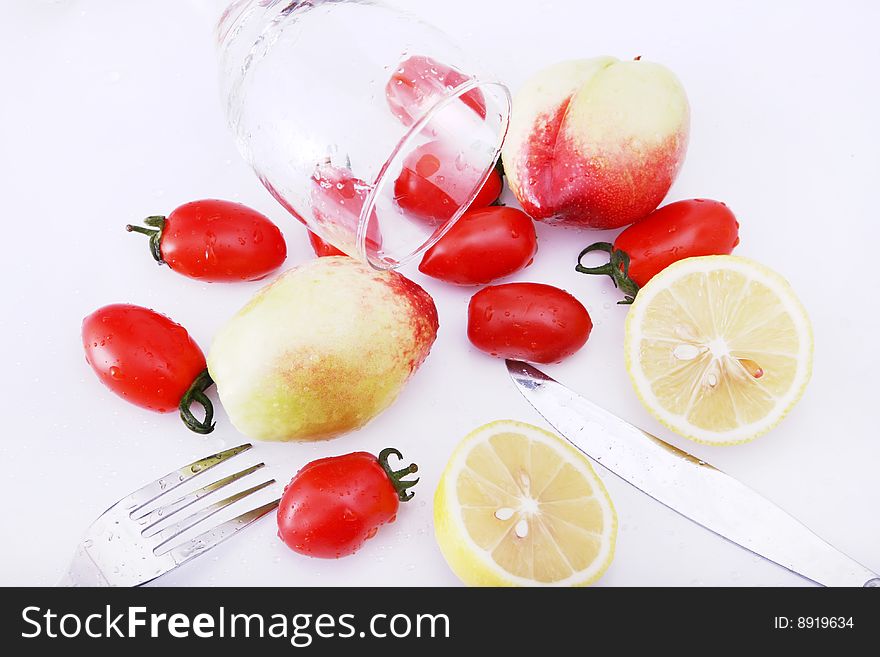 Peachs , peper and lemon tomatoes on white background with goblet, water in it, fork, knife on dest. Peachs , peper and lemon tomatoes on white background with goblet, water in it, fork, knife on dest