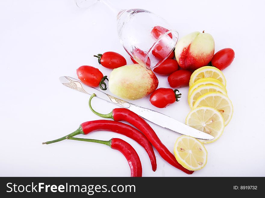 Peachs , peper , lemon and tomatoes on white background with goblet, water in it, knife on desk. Peachs , peper , lemon and tomatoes on white background with goblet, water in it, knife on desk