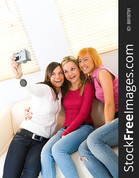 Three happy girls sitting on couch. One of them taking a picture. Three happy girls sitting on couch. One of them taking a picture.