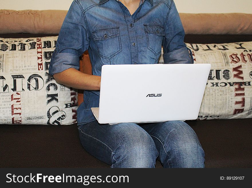 A woman sitting on sofa with denim outfit using a white laptop computer. A woman sitting on sofa with denim outfit using a white laptop computer.