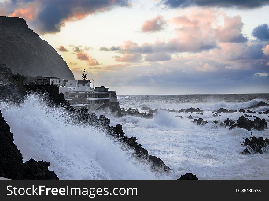 A view of a coast with houses and stormy weather with waves hitting the rocks. A view of a coast with houses and stormy weather with waves hitting the rocks.