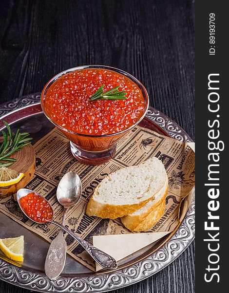A cup of red fish roe and slices of bread and lemon with rosemary on a serving tray. A cup of red fish roe and slices of bread and lemon with rosemary on a serving tray.