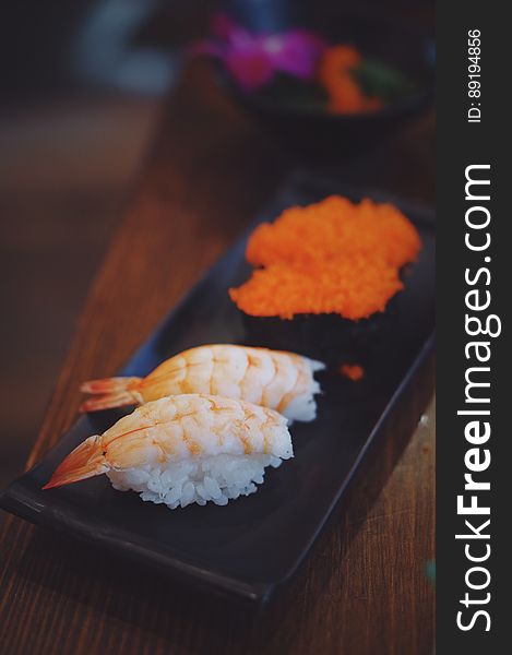 Close up of fresh prawns and salmon sushi on black plate on wooden table. Close up of fresh prawns and salmon sushi on black plate on wooden table.