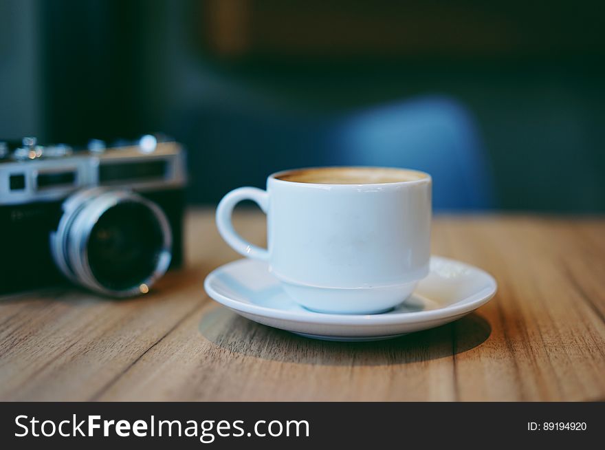 Still life of white china coffee cup and saucer on wooden tabletop with camera. Still life of white china coffee cup and saucer on wooden tabletop with camera.