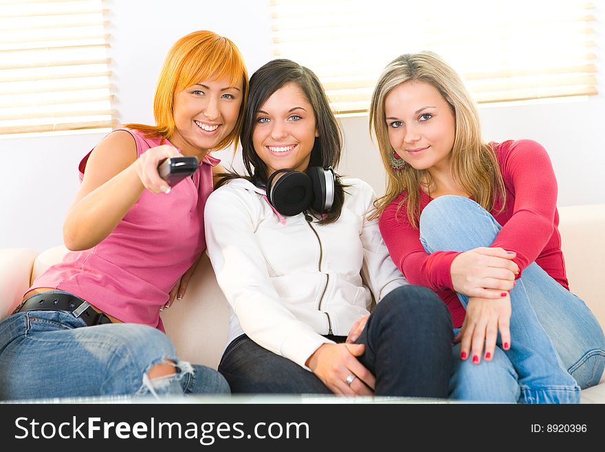 Three girls sitting on couch and smiling. One of them holding control remote. Front view. Three girls sitting on couch and smiling. One of them holding control remote. Front view.