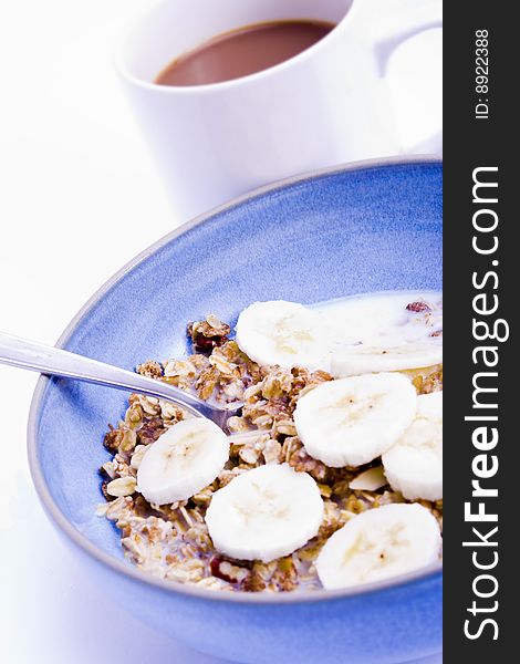 A blue bowl of muesli with bananas and a coffee. A blue bowl of muesli with bananas and a coffee