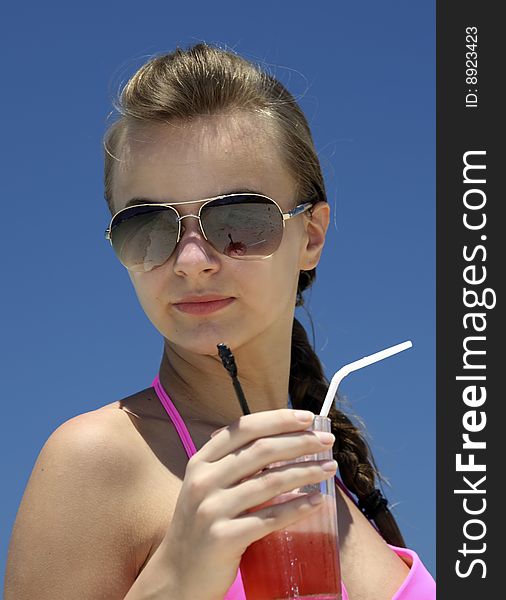 The young woman with juice on a beach against the blue sky. The young woman with juice on a beach against the blue sky