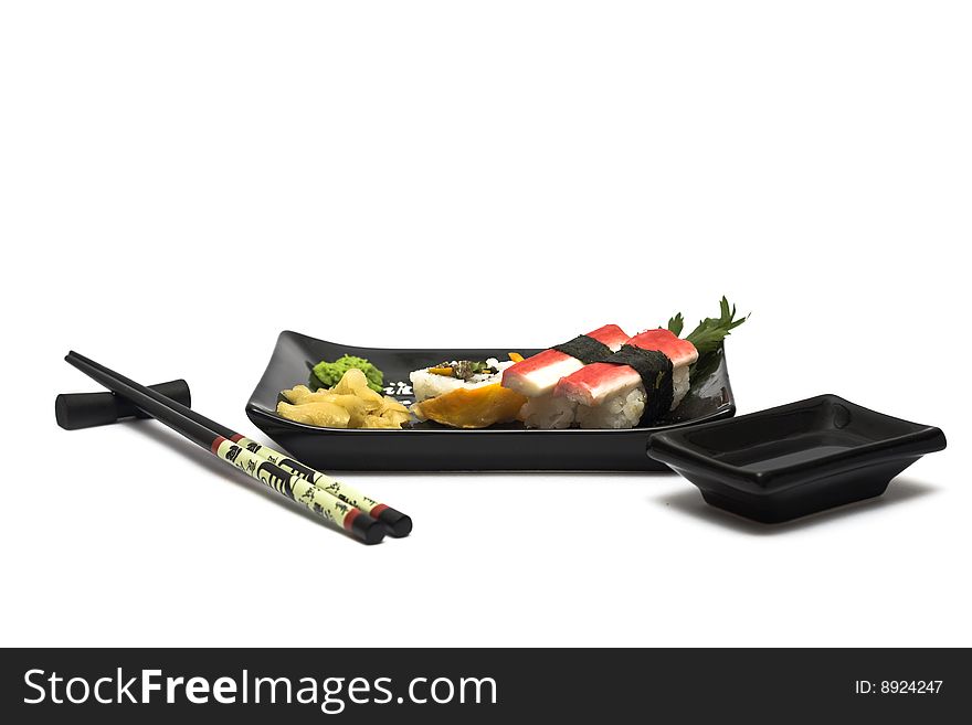 A set of sushi on a black plate with wasabi and gari, isolated on a white background, wish hashi ans soy sauce. A set of sushi on a black plate with wasabi and gari, isolated on a white background, wish hashi ans soy sauce.
