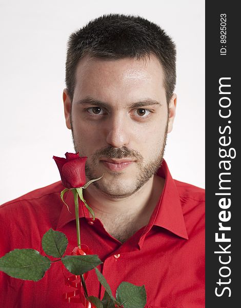 Young, handsome man in red shirt, holding a beautiful red rose in front of him, smiling mysteriously. Young, handsome man in red shirt, holding a beautiful red rose in front of him, smiling mysteriously