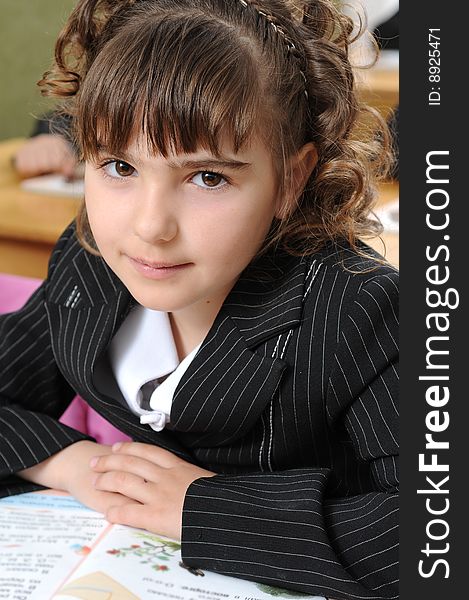 The girl the first-grader sits at school at a lesson and modestly smiles. The girl the first-grader sits at school at a lesson and modestly smiles.