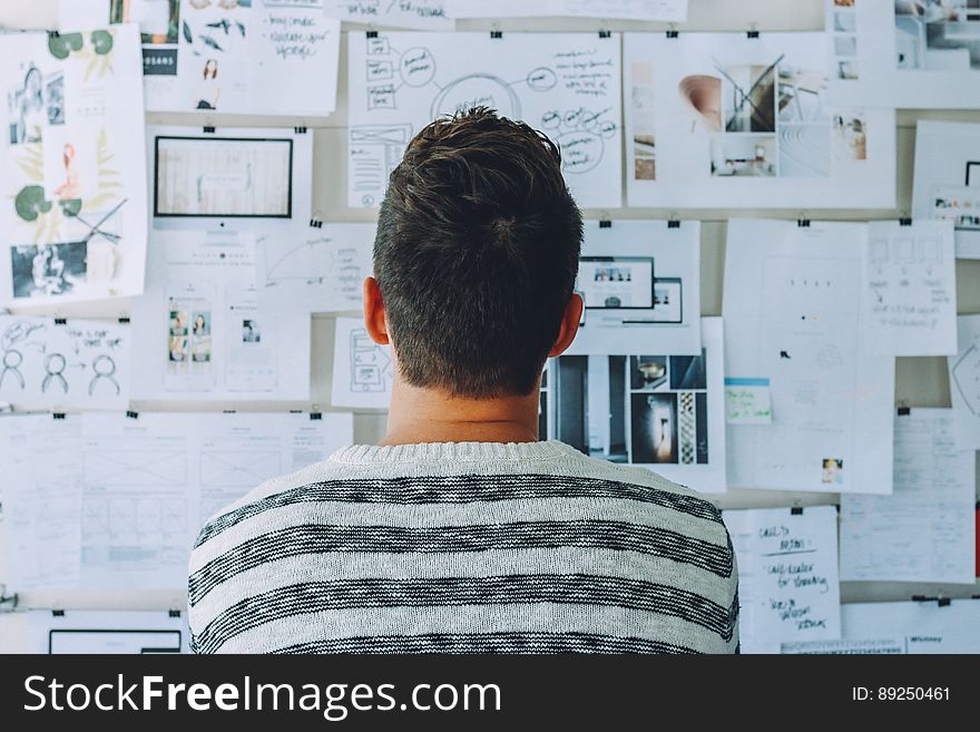 Man Wearing Black and White Stripe Shirt Looking at White Printer Papers on the Wall