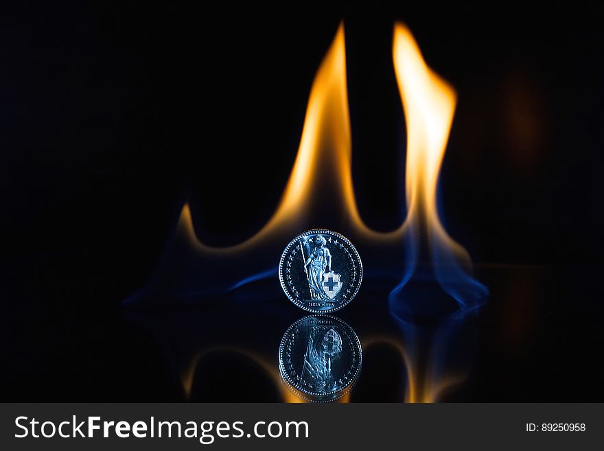 A coin on black background with flames rising on the background. A coin on black background with flames rising on the background.