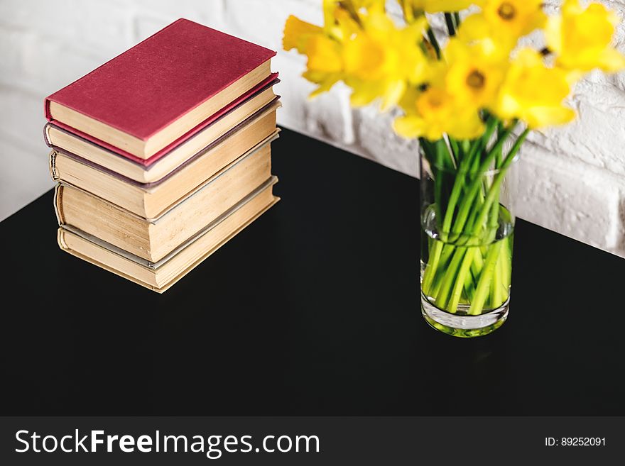 A table with books and yellow daffodils in a vase. A table with books and yellow daffodils in a vase.