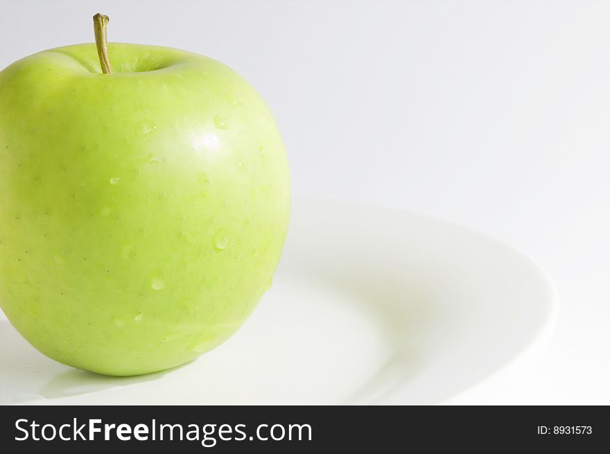 Single fresh, green apple, slightly cropped, on dish with white background. Horizontal image with copy-space. Single fresh, green apple, slightly cropped, on dish with white background. Horizontal image with copy-space