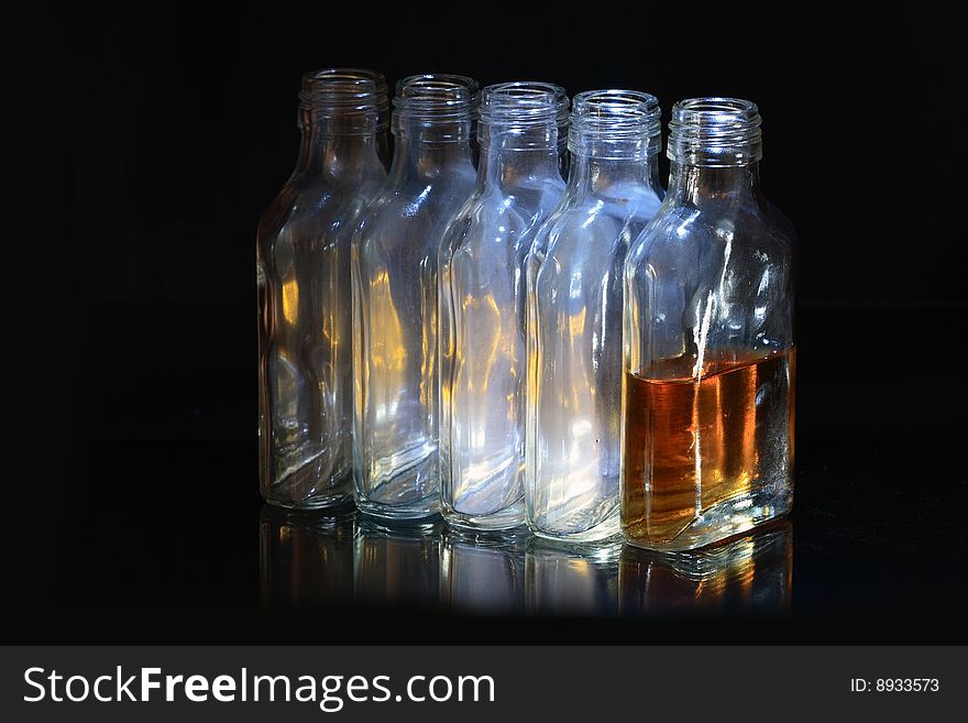 Four empty and one bottle with cognac on dark background. Four empty and one bottle with cognac on dark background