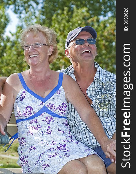 Aged couple sitting on a bench and laughing out loud