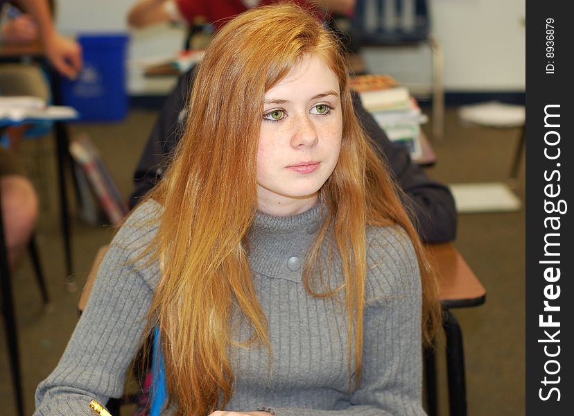 Strawberry blonde teenager taking notes in a classroom. Strawberry blonde teenager taking notes in a classroom