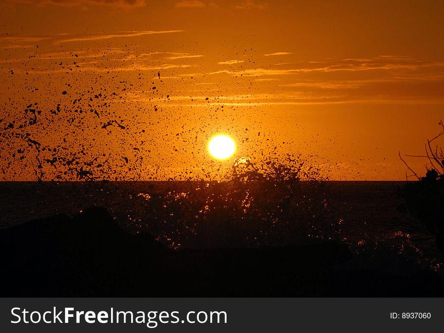 A beautiful, orange sunset with waves crashing in the foreground.