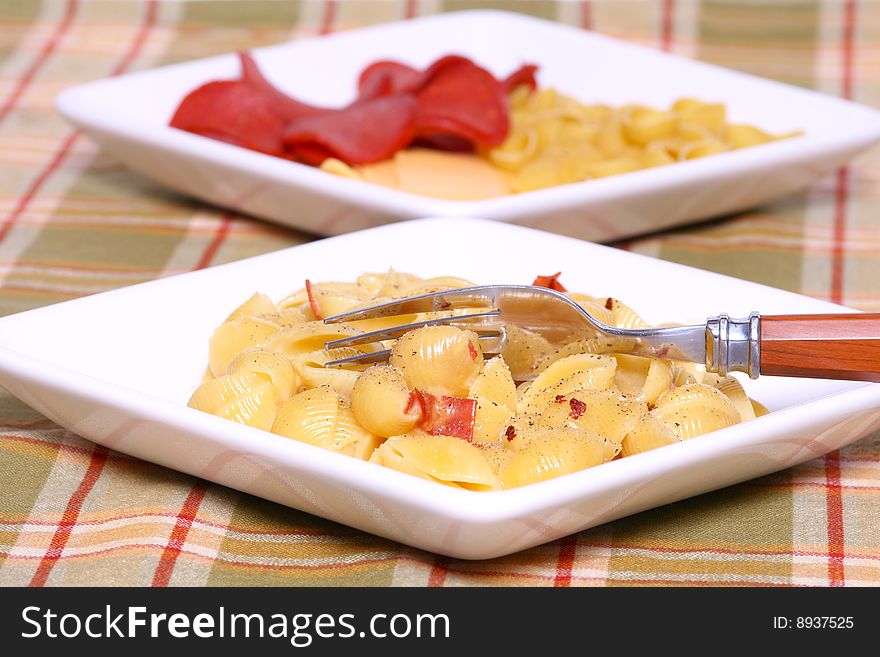 Macaroni and pepperoni on a white plate with ingredients in the background with fork