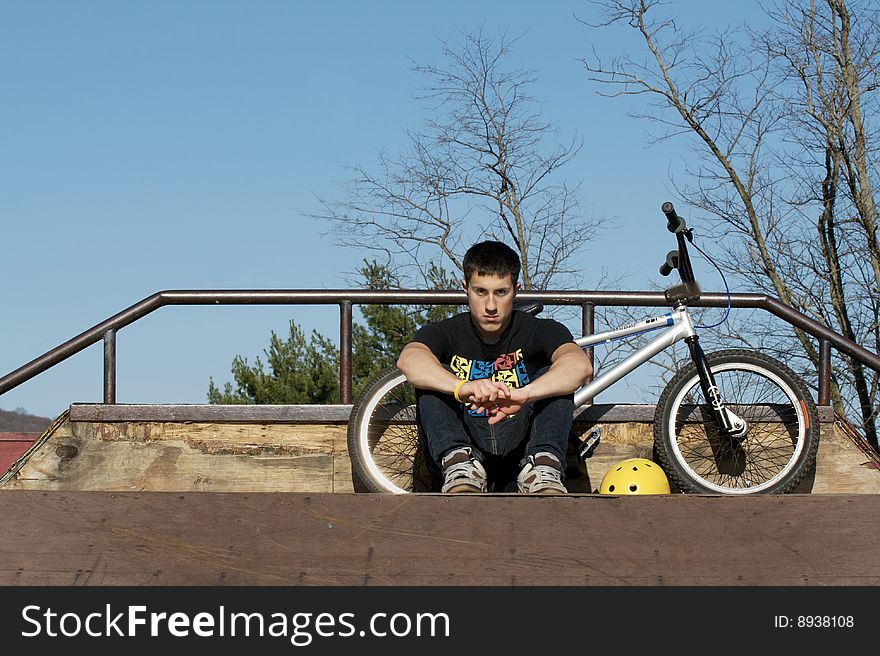 A teenage Bmx rider, takes a rest at a skate park. A teenage Bmx rider, takes a rest at a skate park.