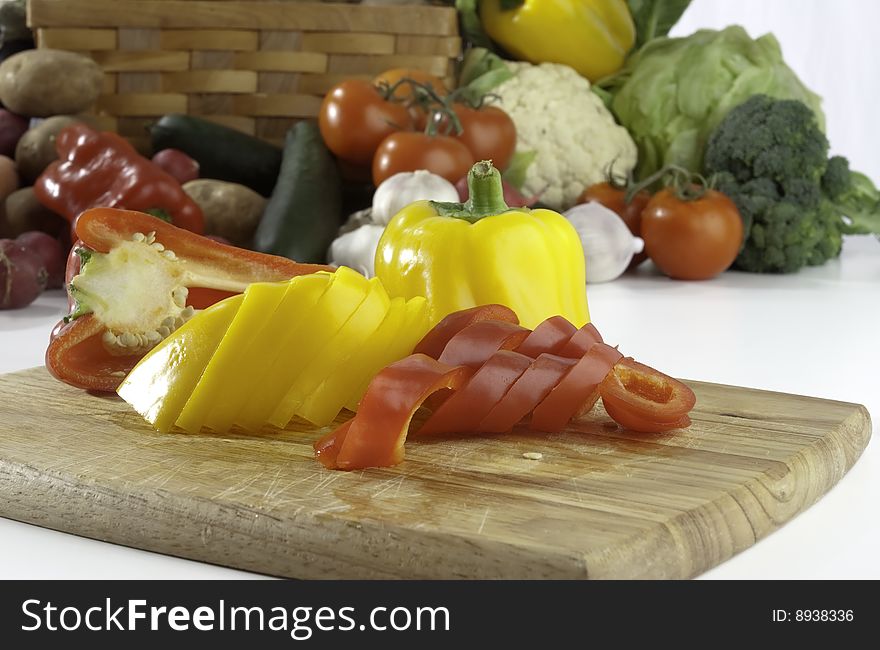 Fresh sliced peppers on wooden background with vegetables on the background